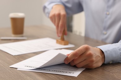 Photo of Man stamping licensing agreement document at wooden table indoors, closeup