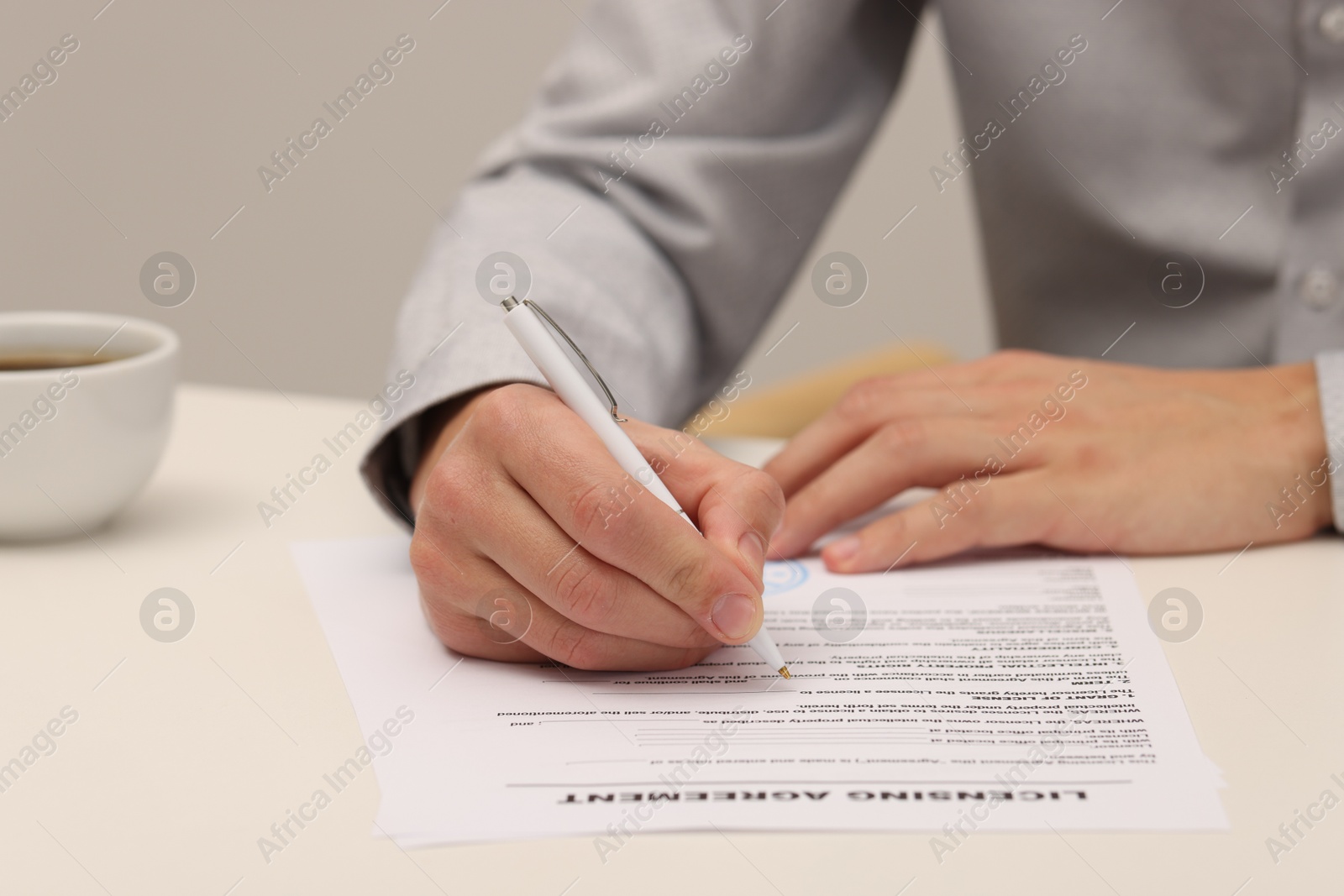 Photo of Man signing licensing agreement document at white table indoors, closeup