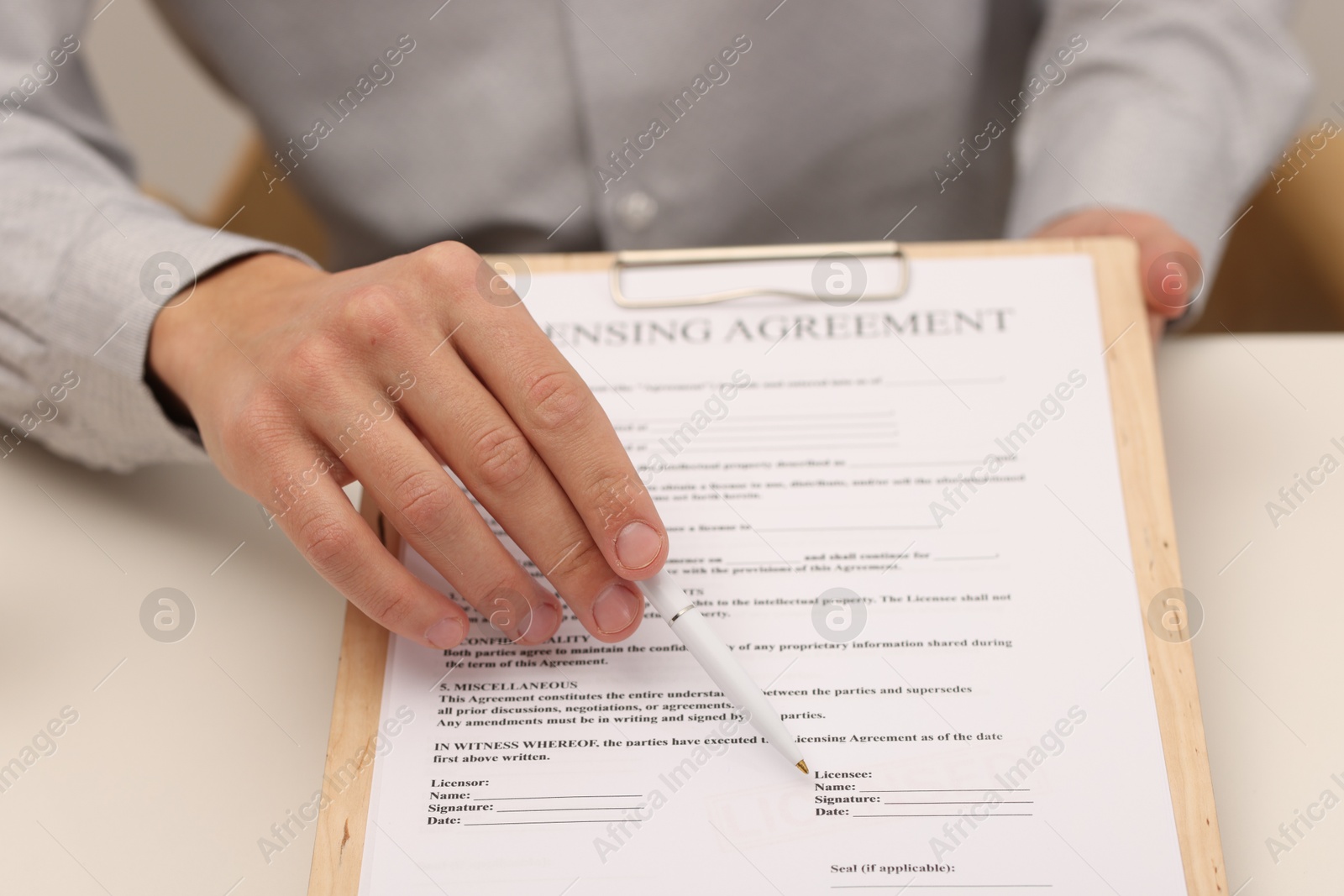 Photo of Man with pen pointing licensing agreement at document at white table indoors, closeup