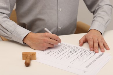 Photo of Man signing licensing agreement document at white table indoors, closeup