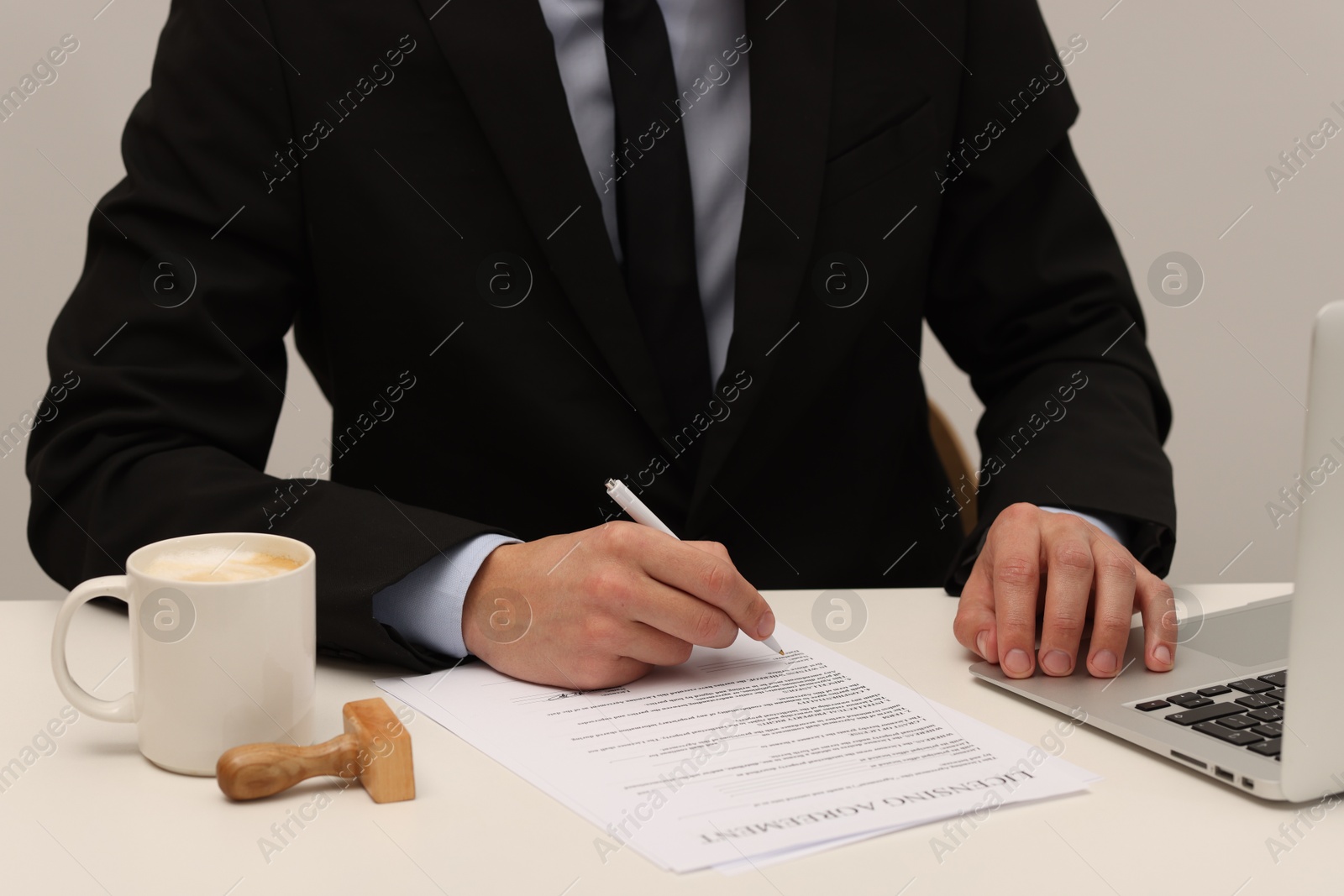 Photo of Man signing licensing agreement document at white table indoors, closeup