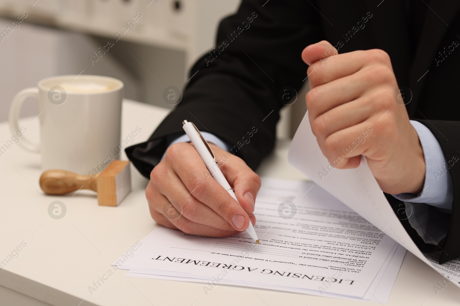 Photo of Man signing licensing agreement document at white table indoors, closeup