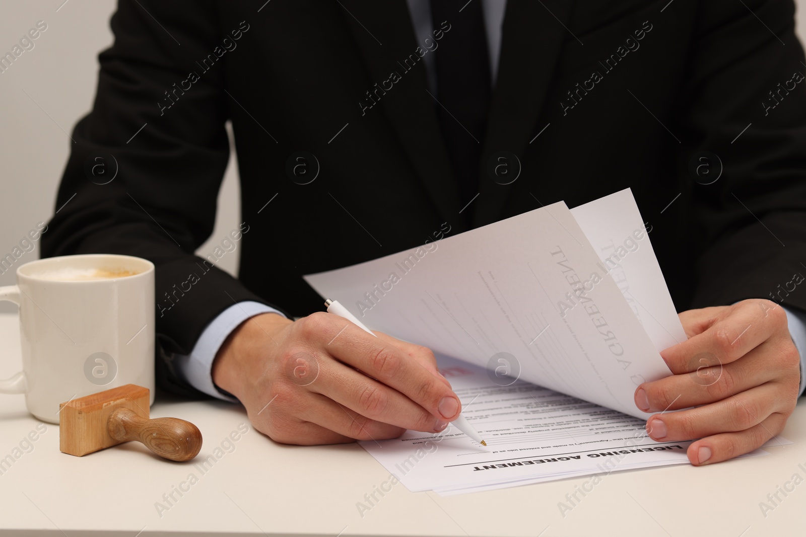 Photo of Man signing licensing agreement document at white table indoors, closeup