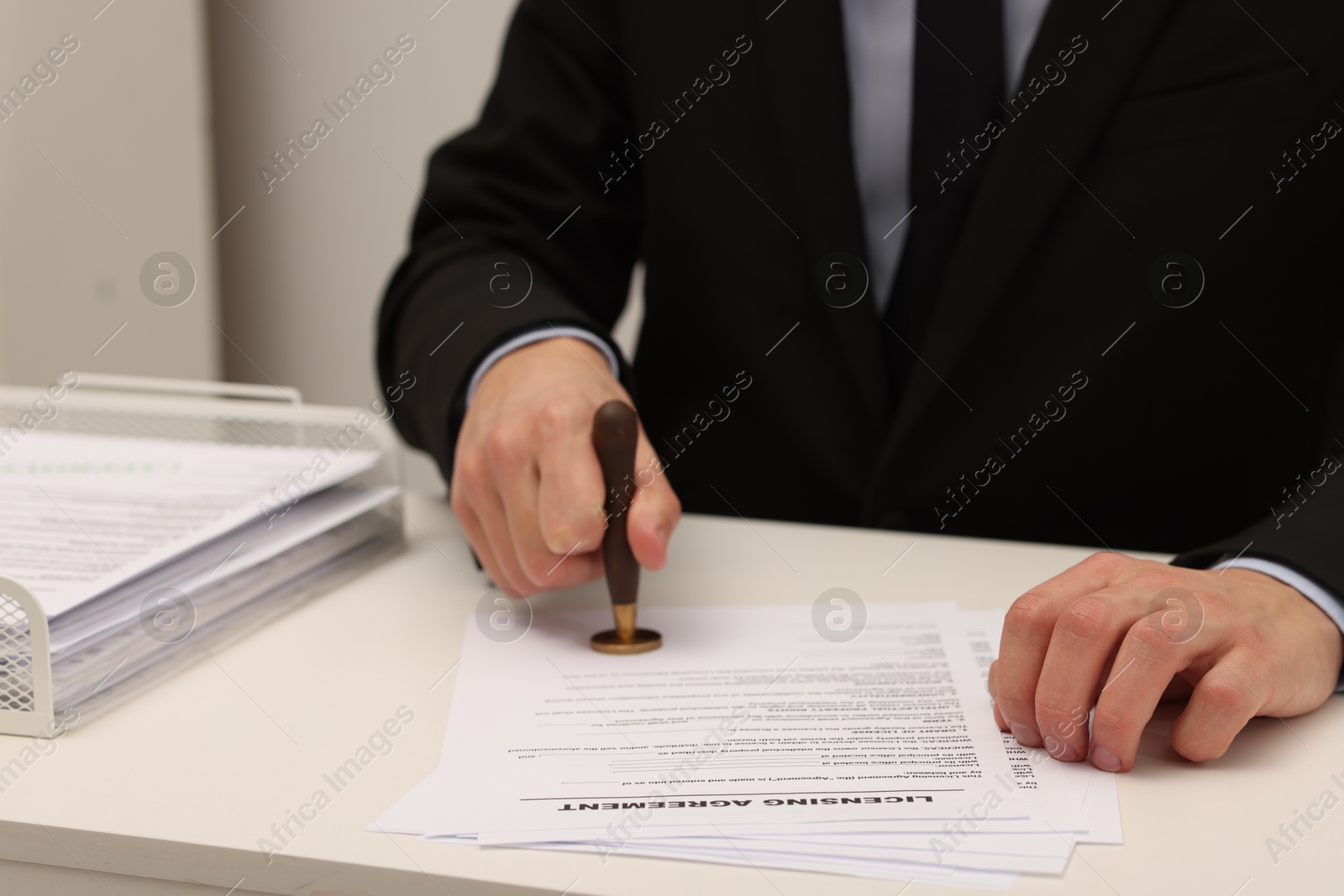 Photo of Man stamping licensing agreement document at white table indoors, closeup