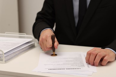 Photo of Man stamping licensing agreement document at white table indoors, closeup