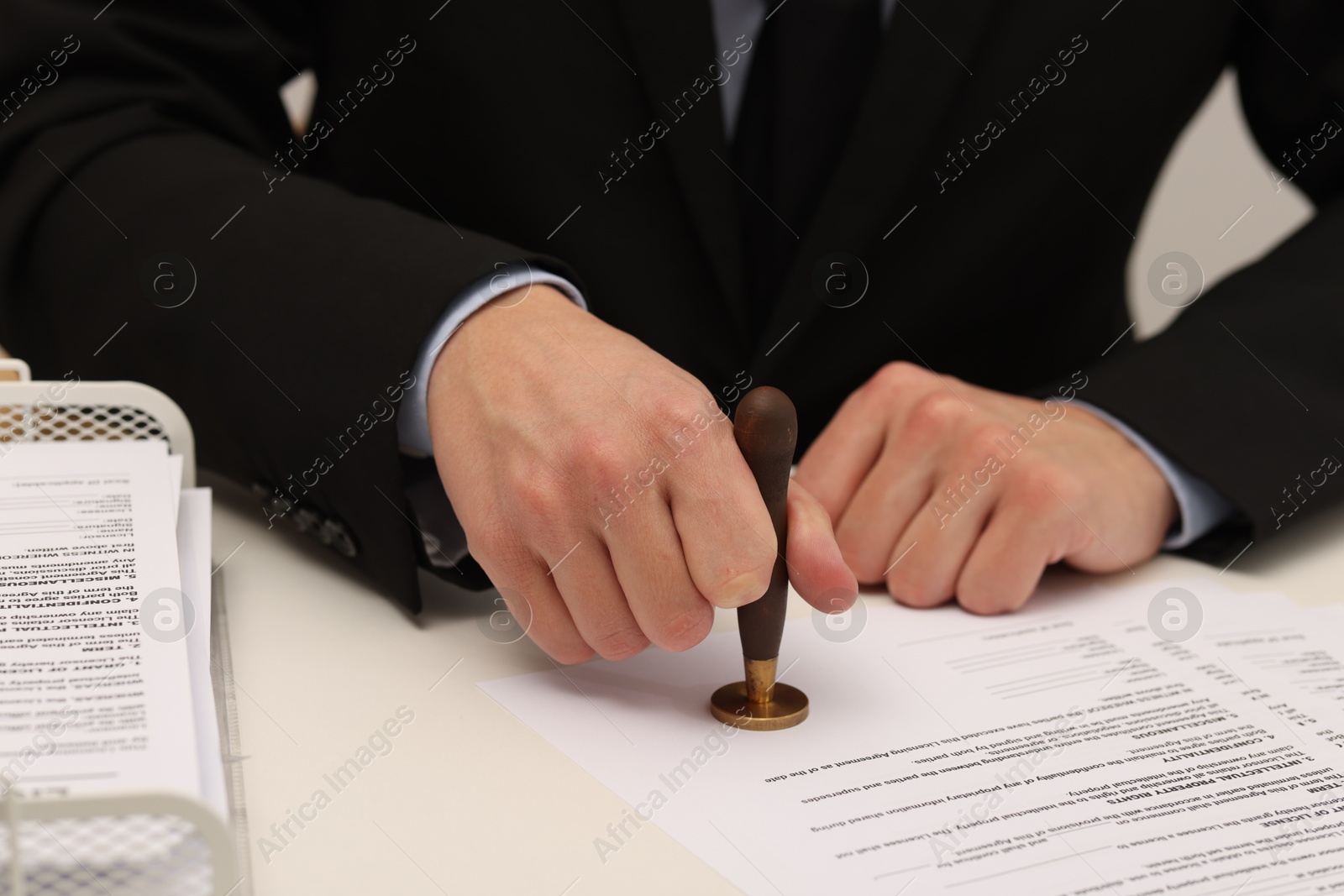 Photo of Man stamping licensing agreement document at white table indoors, closeup