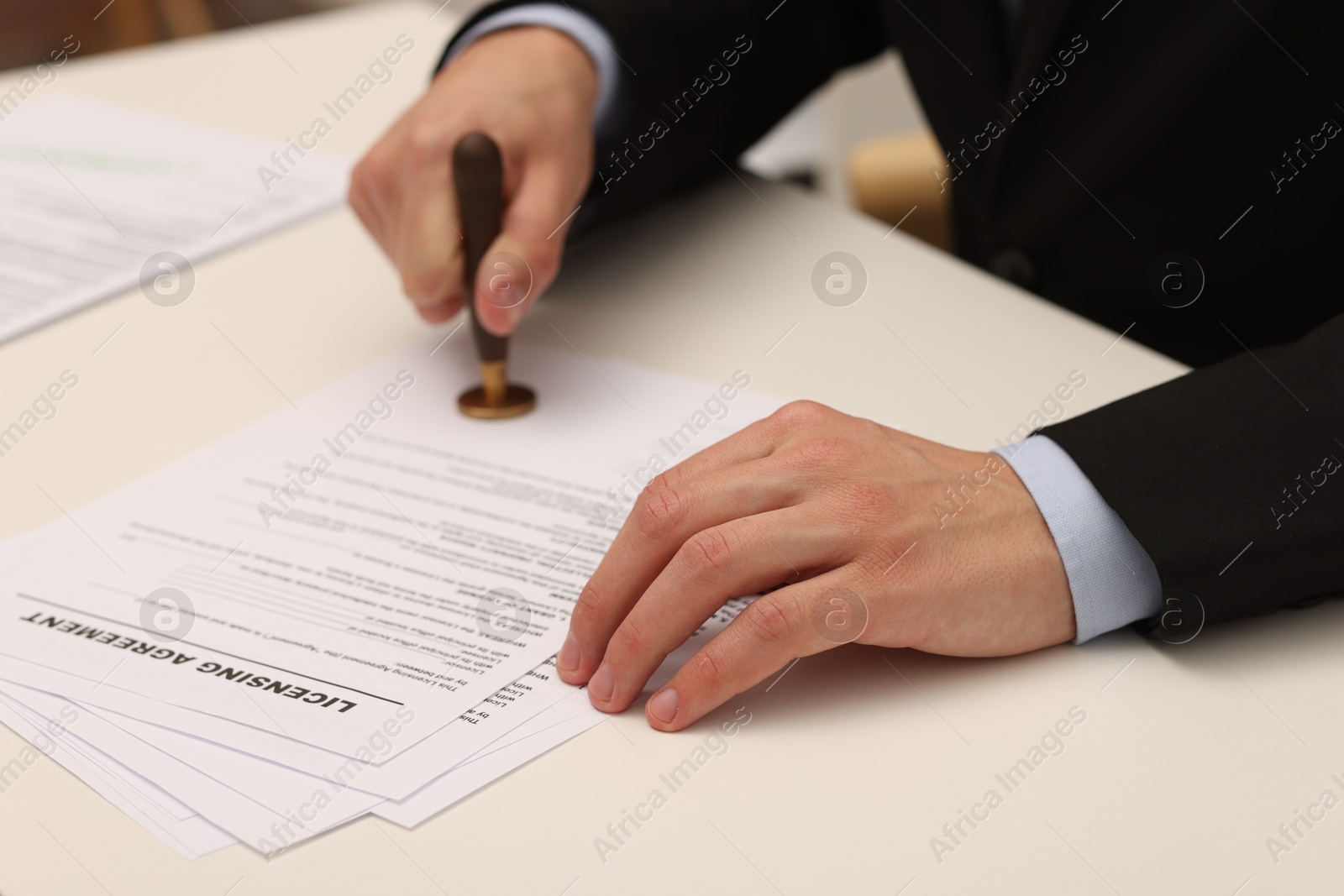 Photo of Man stamping licensing agreement document at white table indoors, closeup