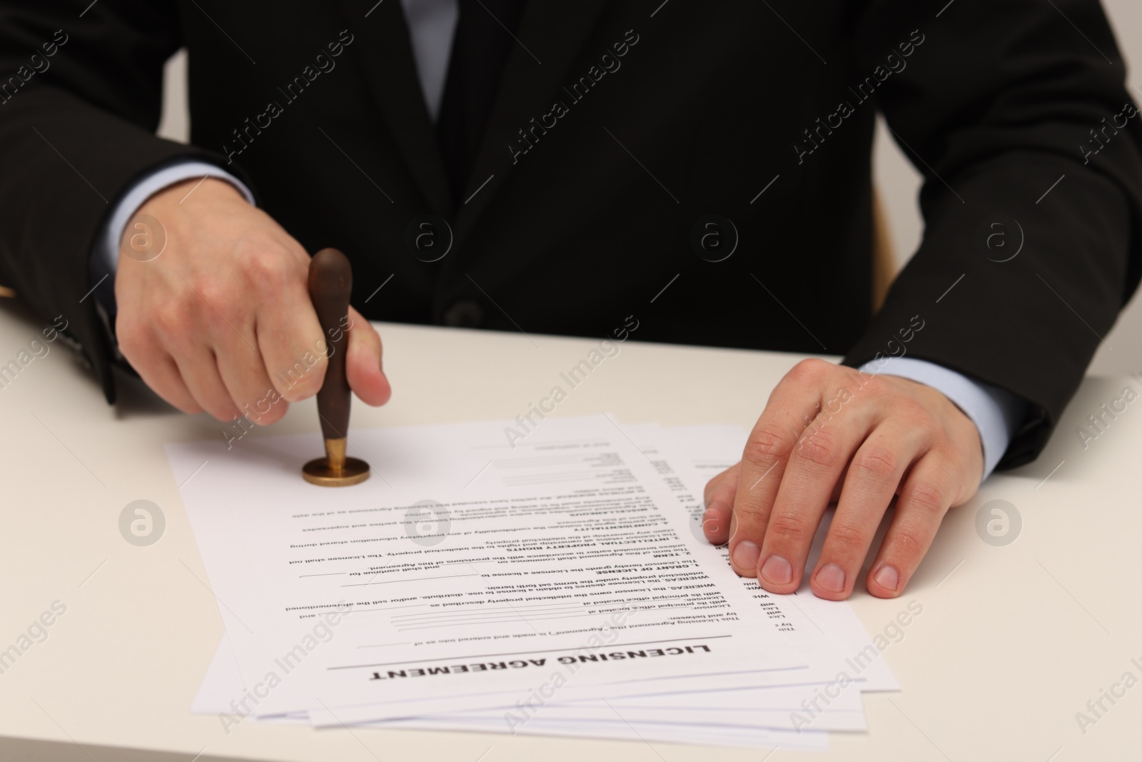 Photo of Man stamping licensing agreement document at white table indoors, closeup