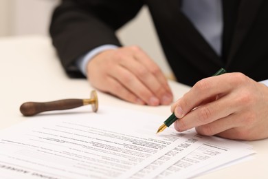 Photo of Man signing licensing agreement document at table indoors, closeup