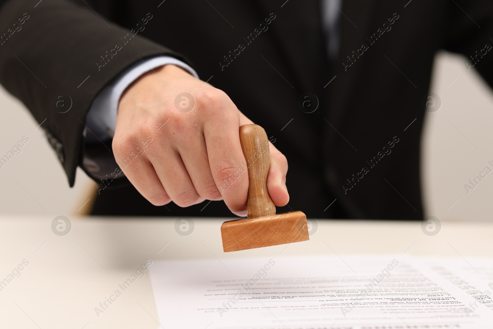 Photo of Man stamping licensing agreement document at white table indoors, closeup