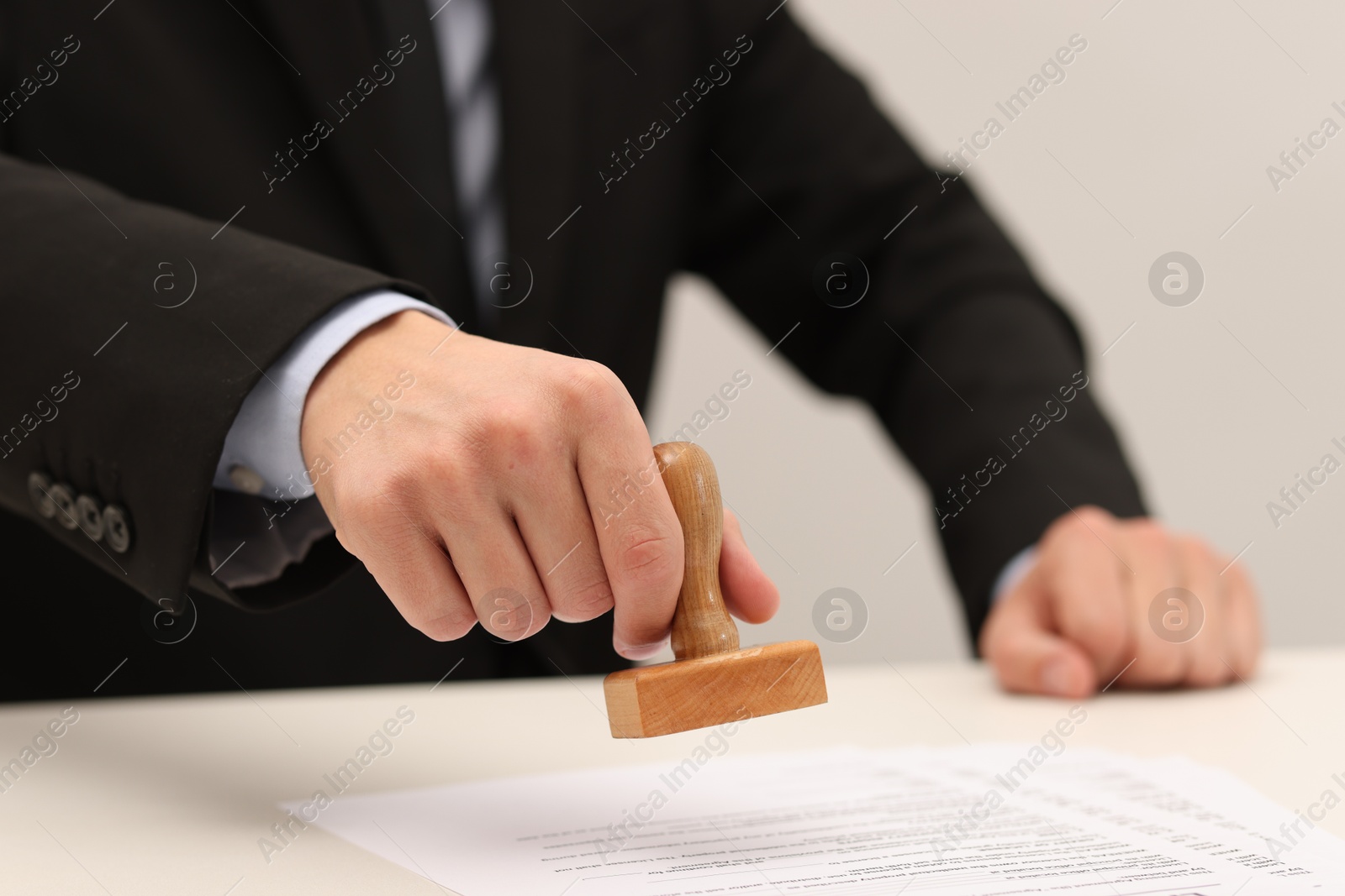 Photo of Man stamping licensing agreement document at white table indoors, closeup