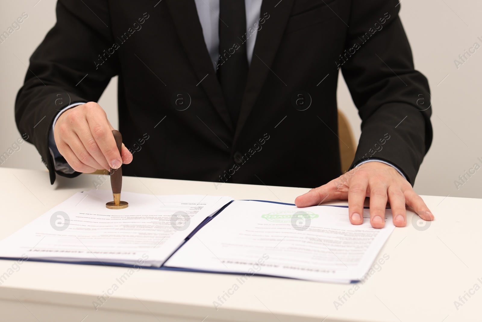 Photo of Man stamping licensing agreement document at white table indoors, closeup