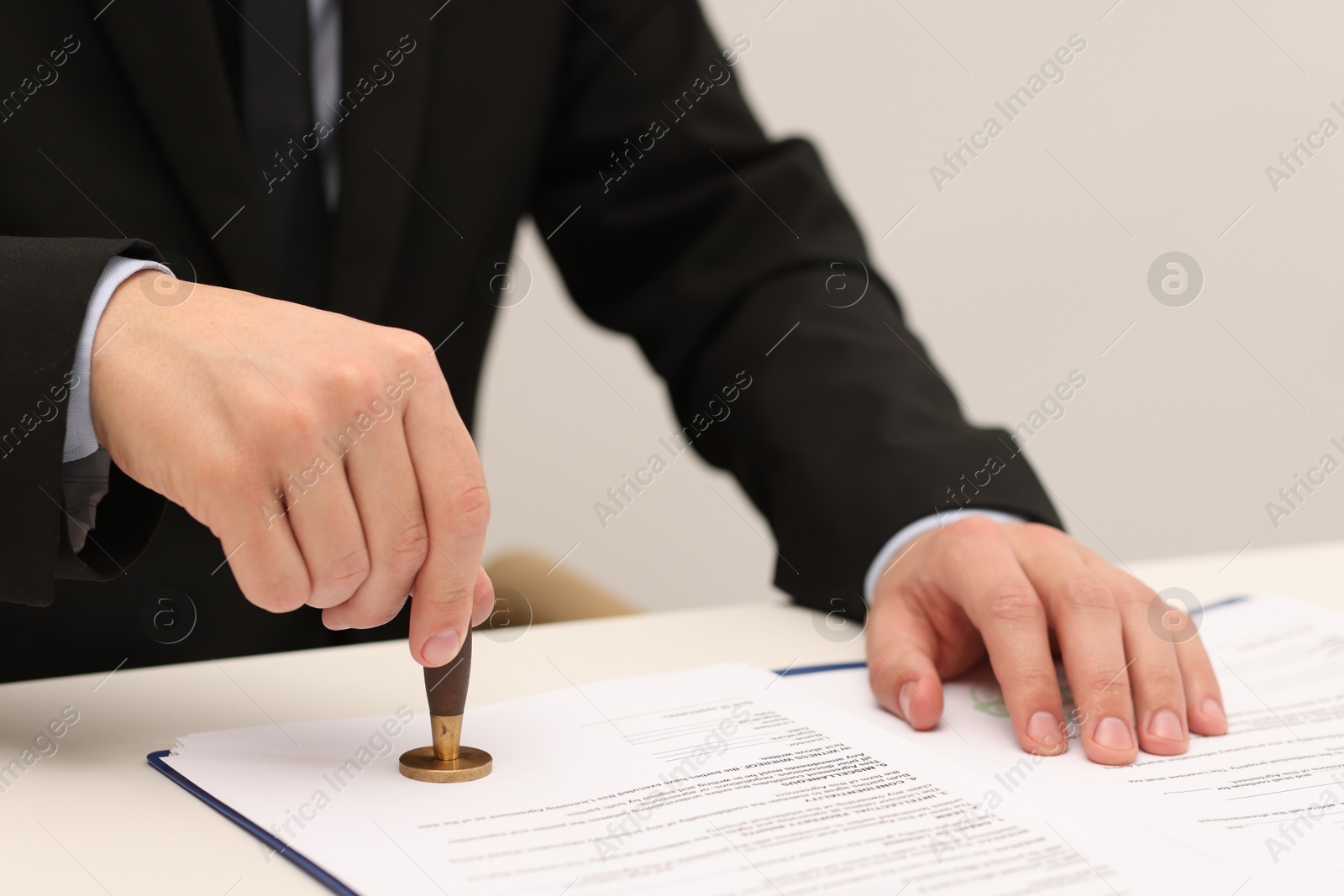 Photo of Man stamping licensing agreement document at white table indoors, closeup