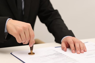 Photo of Man stamping licensing agreement document at white table indoors, closeup