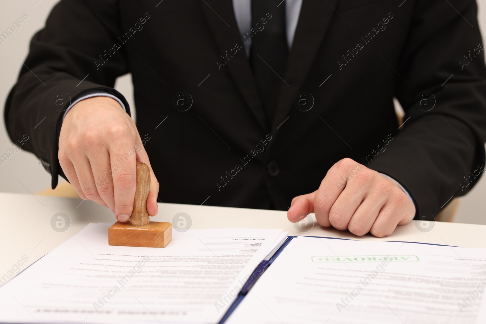 Photo of Man stamping licensing agreement document at white table indoors, closeup