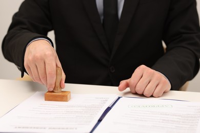 Photo of Man stamping licensing agreement document at white table indoors, closeup