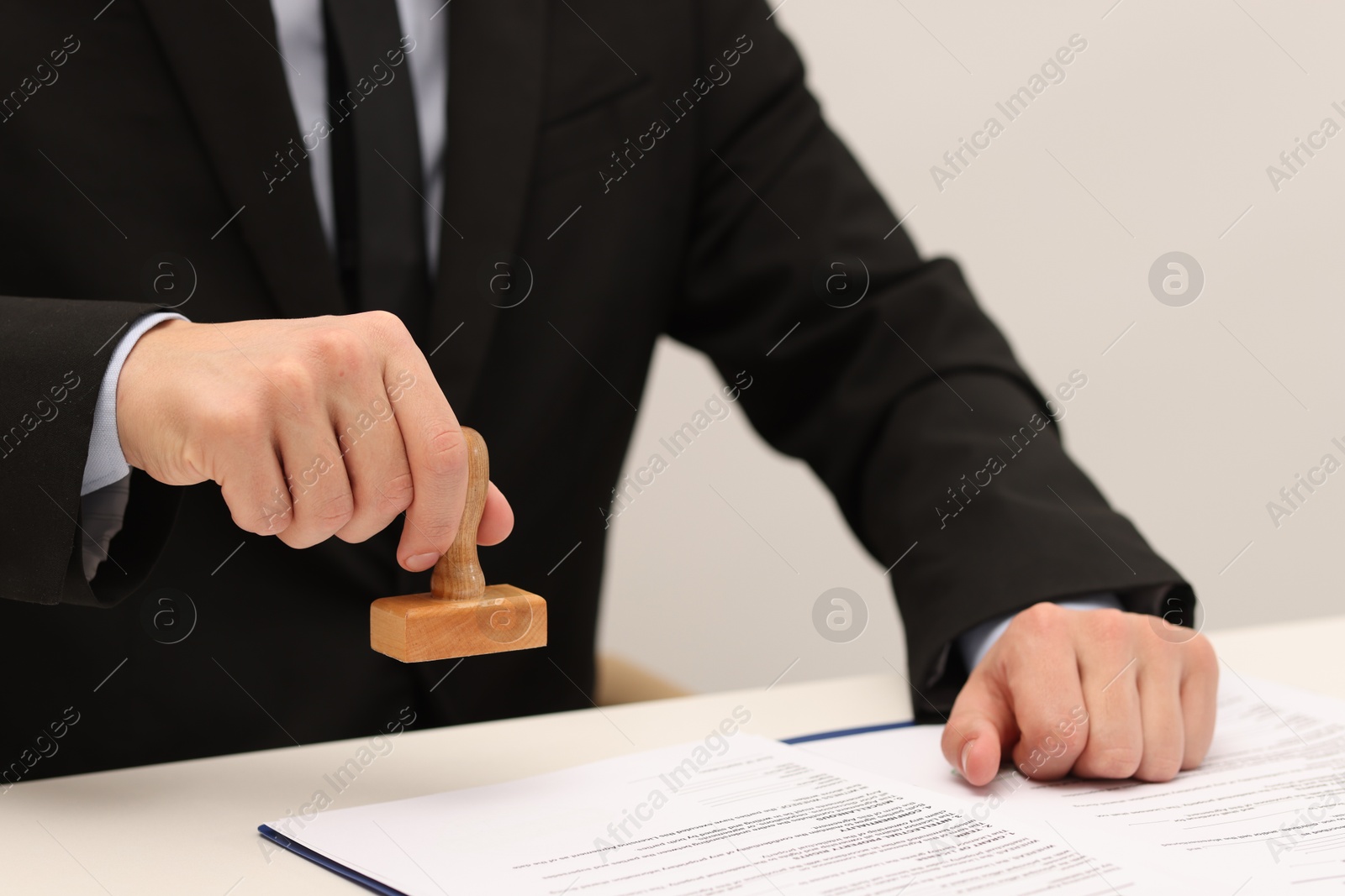 Photo of Man stamping licensing agreement document at white table indoors, closeup