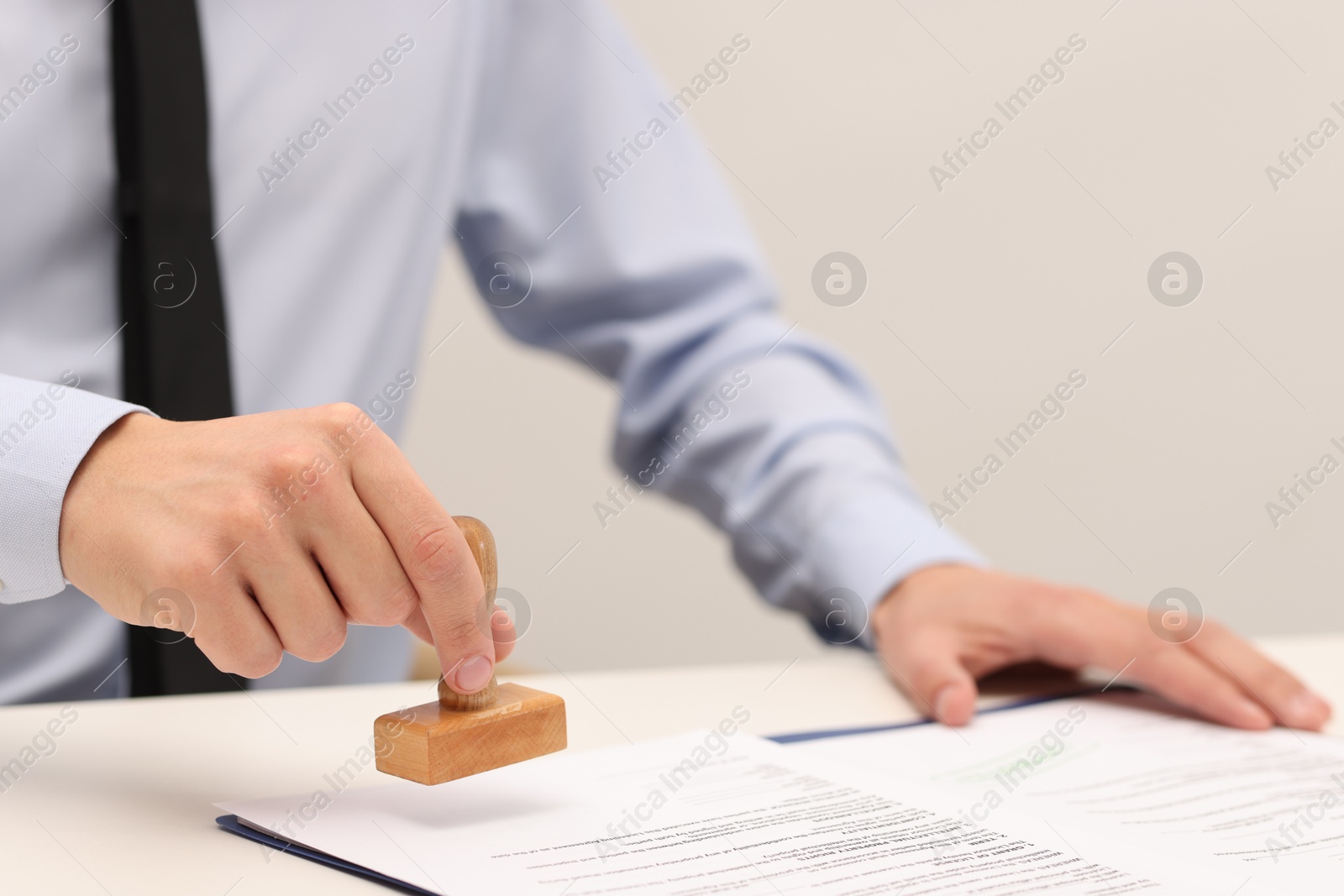 Photo of Man stamping licensing agreement document at white table indoors, closeup