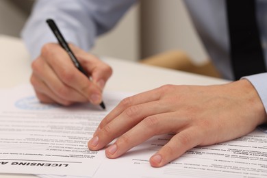 Photo of Man signing licensing agreement document at table indoors, closeup