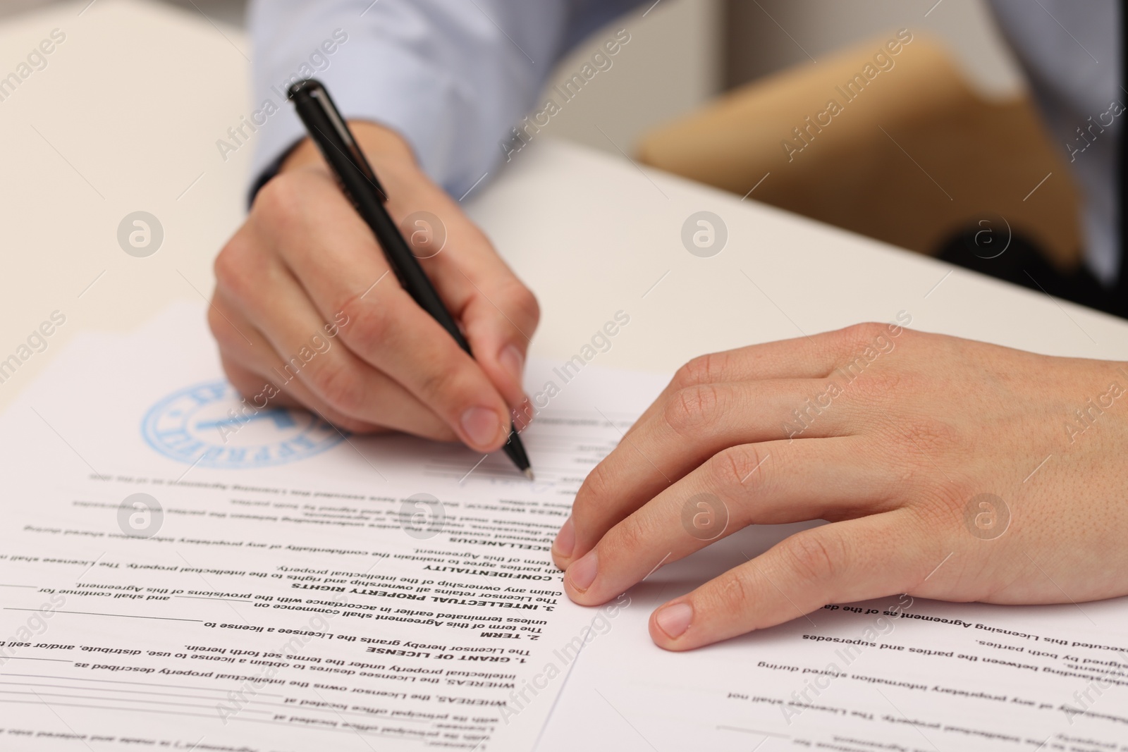 Photo of Man signing licensing agreement document at white table indoors, closeup