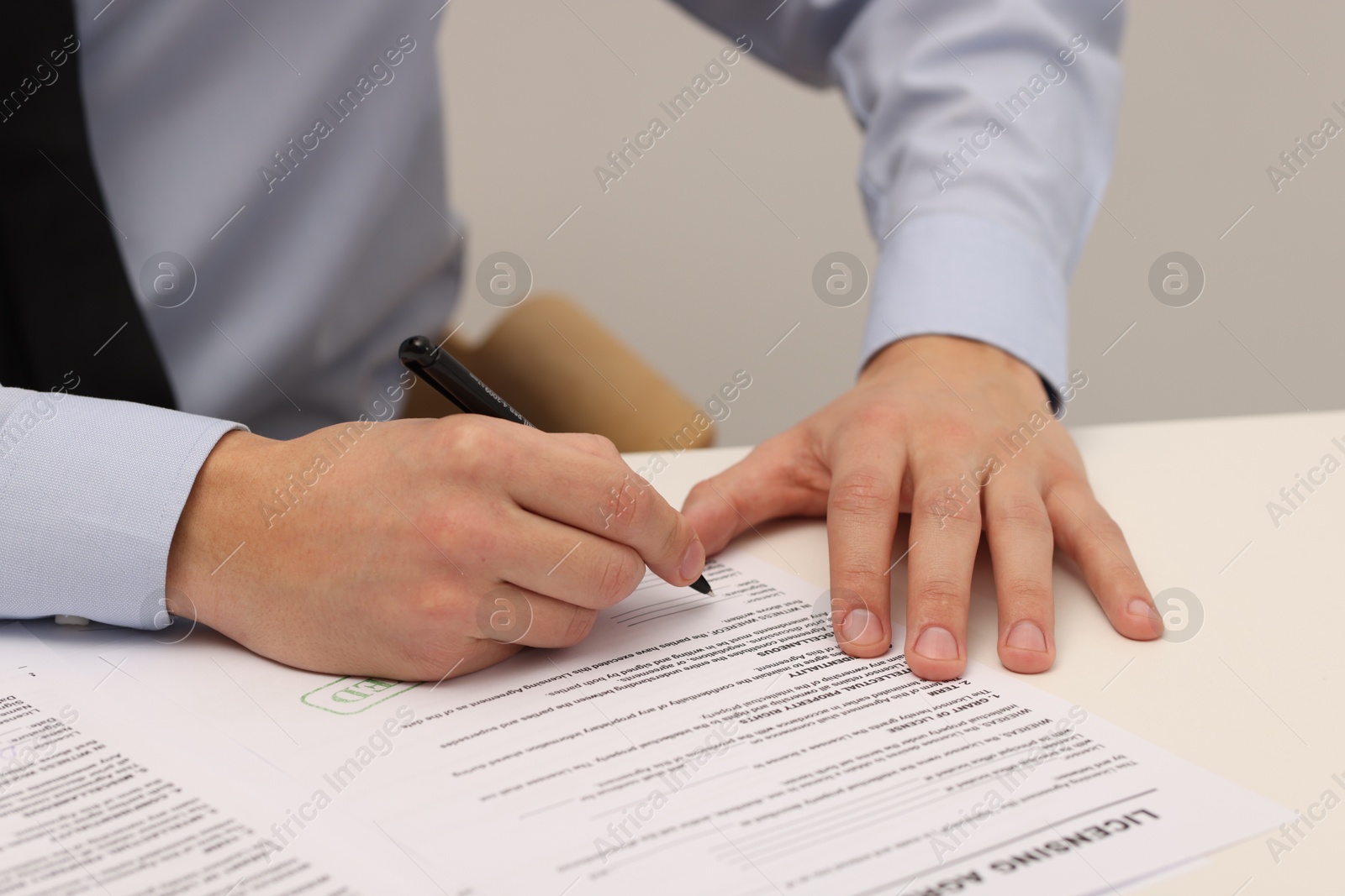 Photo of Man signing licensing agreement document at white table indoors, closeup