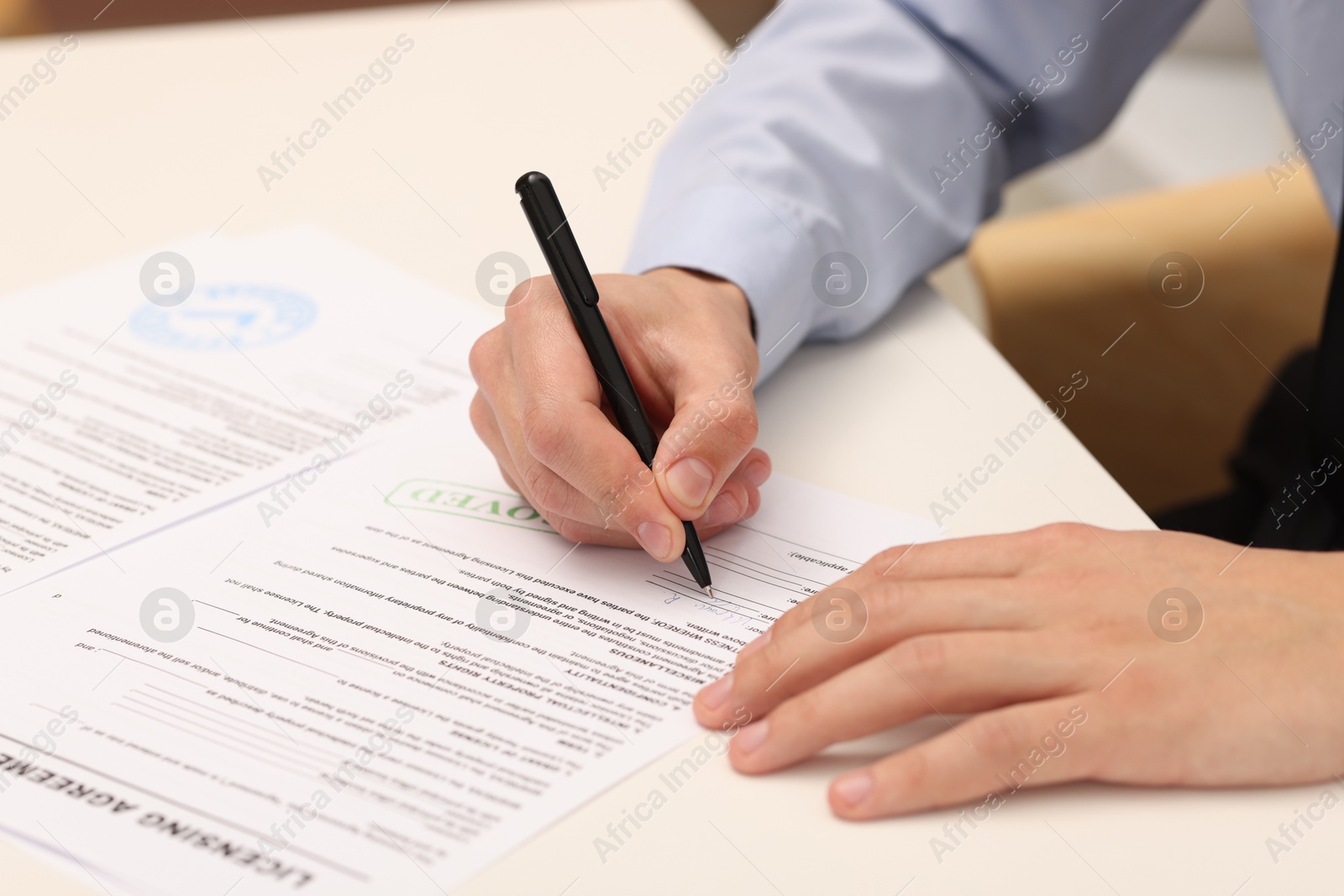 Photo of Man signing licensing agreement document at white table indoors, closeup