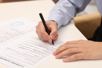 Photo of Man signing licensing agreement document at white table indoors, closeup