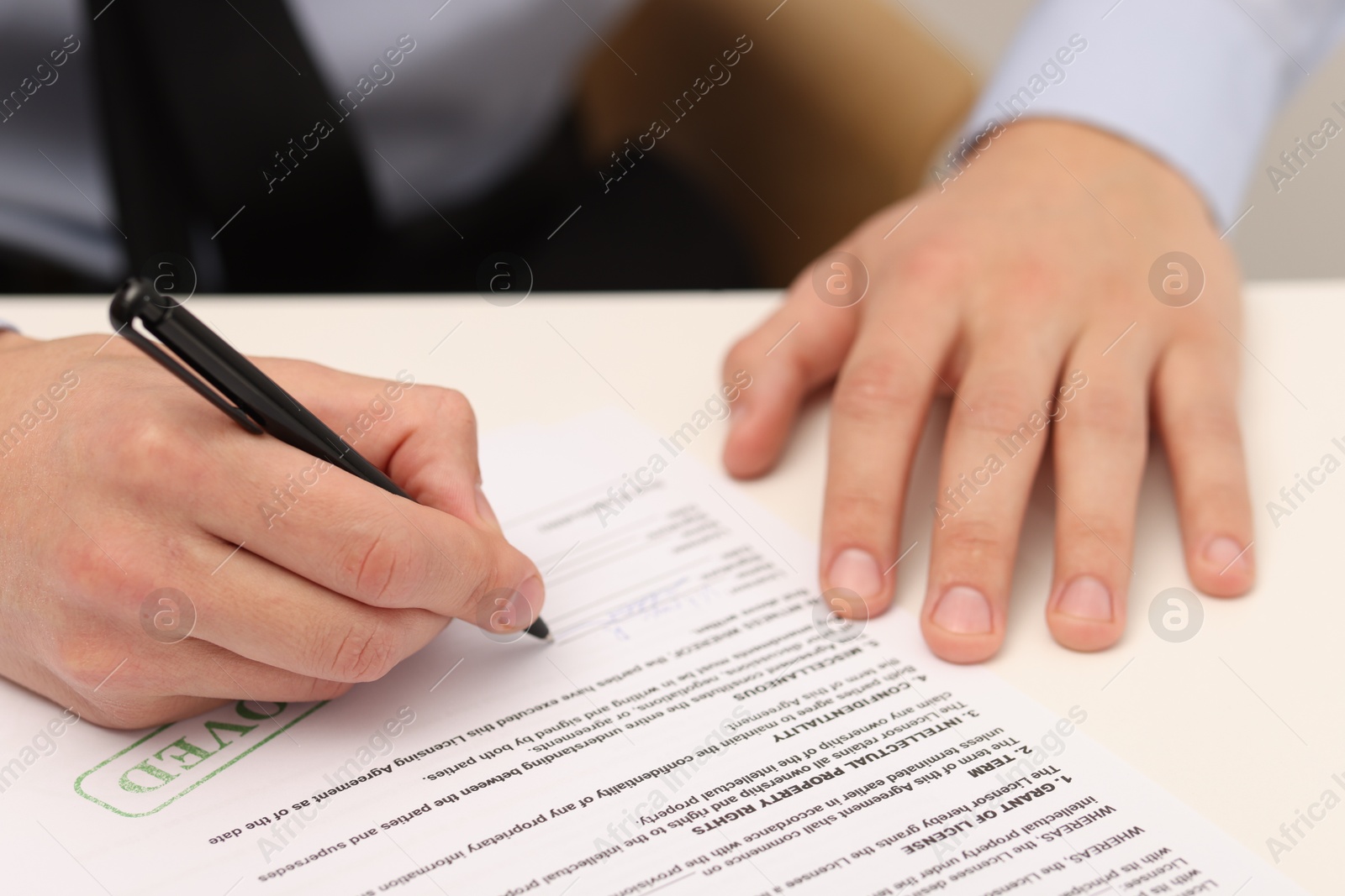 Photo of Man signing licensing agreement document at white table indoors, closeup