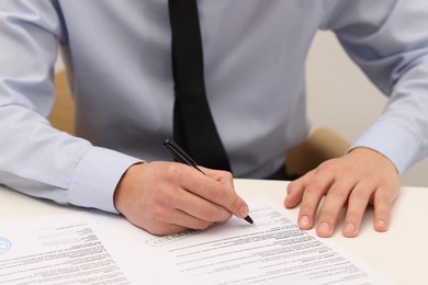 Photo of Man signing licensing agreement document at white table indoors, closeup