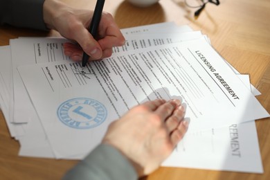 Photo of Woman signing licensing agreement document at wooden table indoors, closeup