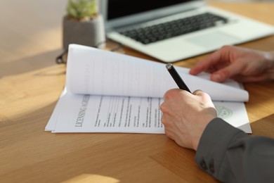 Photo of Woman signing licensing agreement document at wooden table indoors, closeup