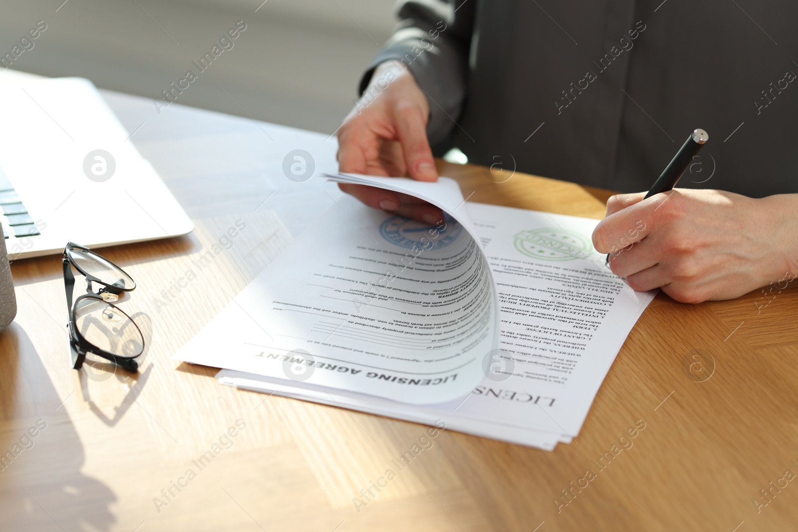 Photo of Woman signing licensing agreement document at wooden table indoors, closeup