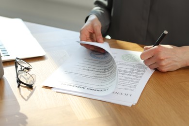 Photo of Woman signing licensing agreement document at wooden table indoors, closeup