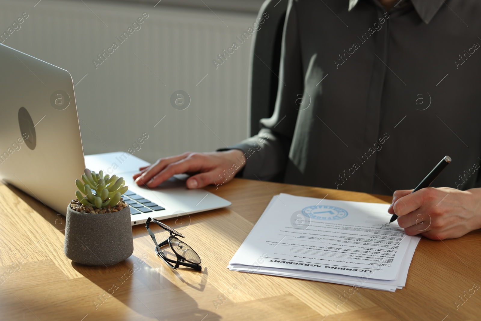 Photo of Woman signing licensing agreement document while working on laptop at wooden table indoors, closeup