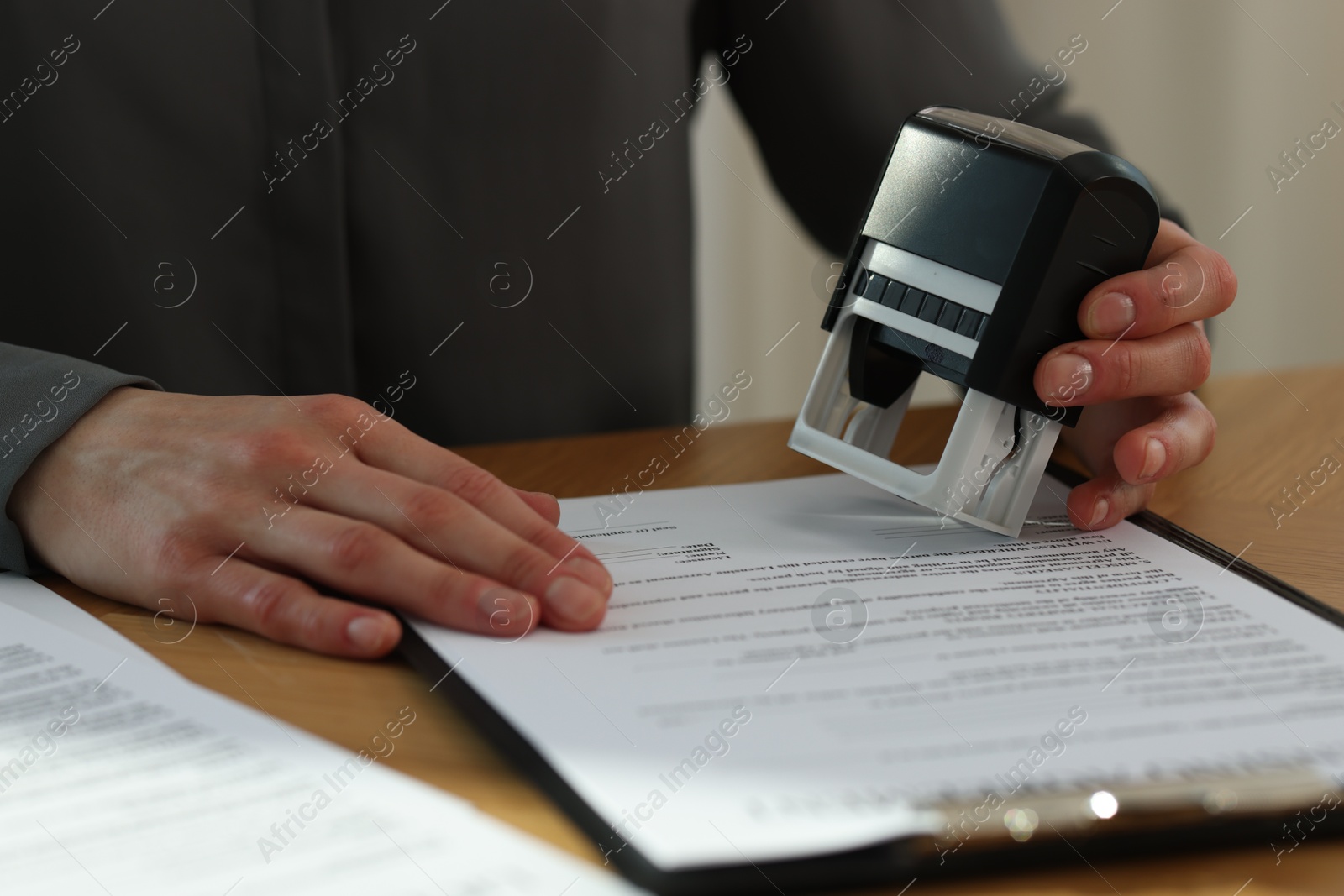 Photo of Woman stamping licensing agreement document at wooden table indoors, closeup