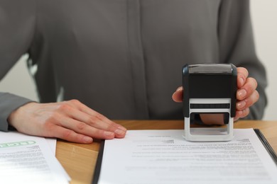 Photo of Woman stamping licensing agreement document at wooden table indoors, closeup