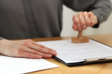 Photo of Woman stamping licensing agreement document at wooden table indoors, closeup