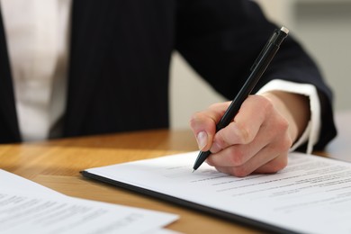 Photo of Woman signing licensing agreement document at wooden table indoors, closeup