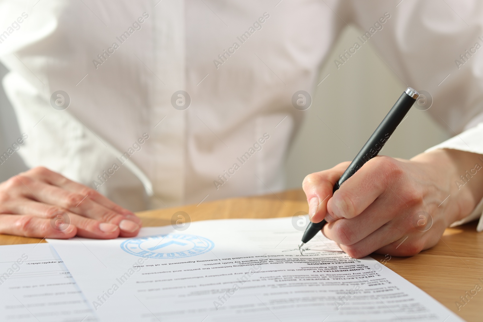 Photo of Woman signing licensing agreement document at wooden table indoors, closeup