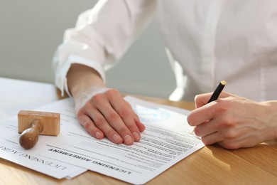 Photo of Woman signing licensing agreement document at wooden table indoors, closeup