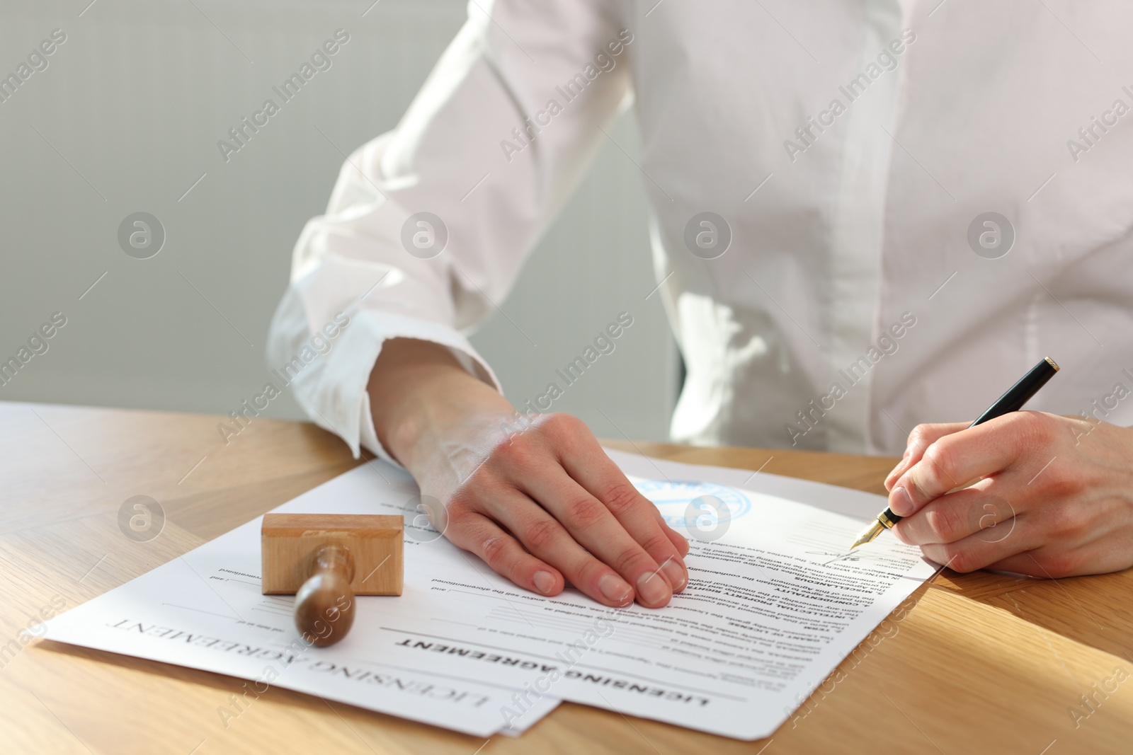 Photo of Woman signing licensing agreement document at wooden table indoors, closeup