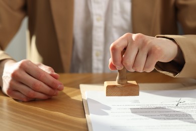 Photo of Woman stamping licensing agreement document at wooden table indoors, closeup