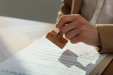 Photo of Woman stamping licensing agreement document at wooden table indoors, closeup