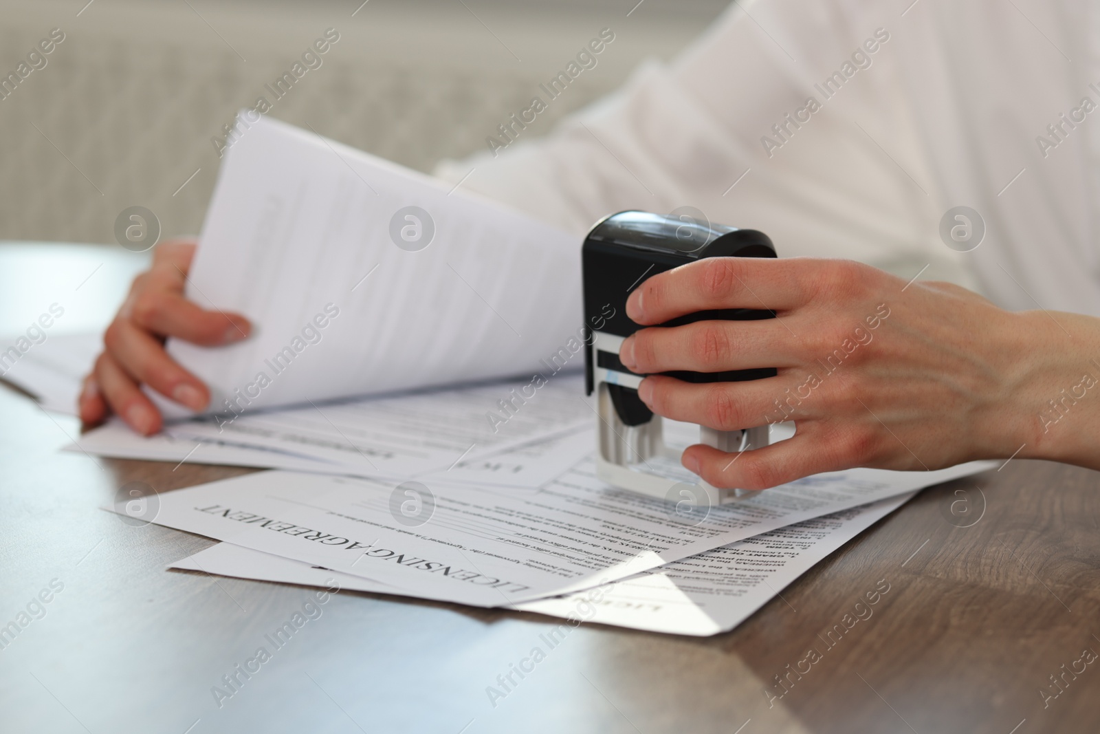 Photo of Woman stamping licensing agreement document at wooden table indoors, closeup