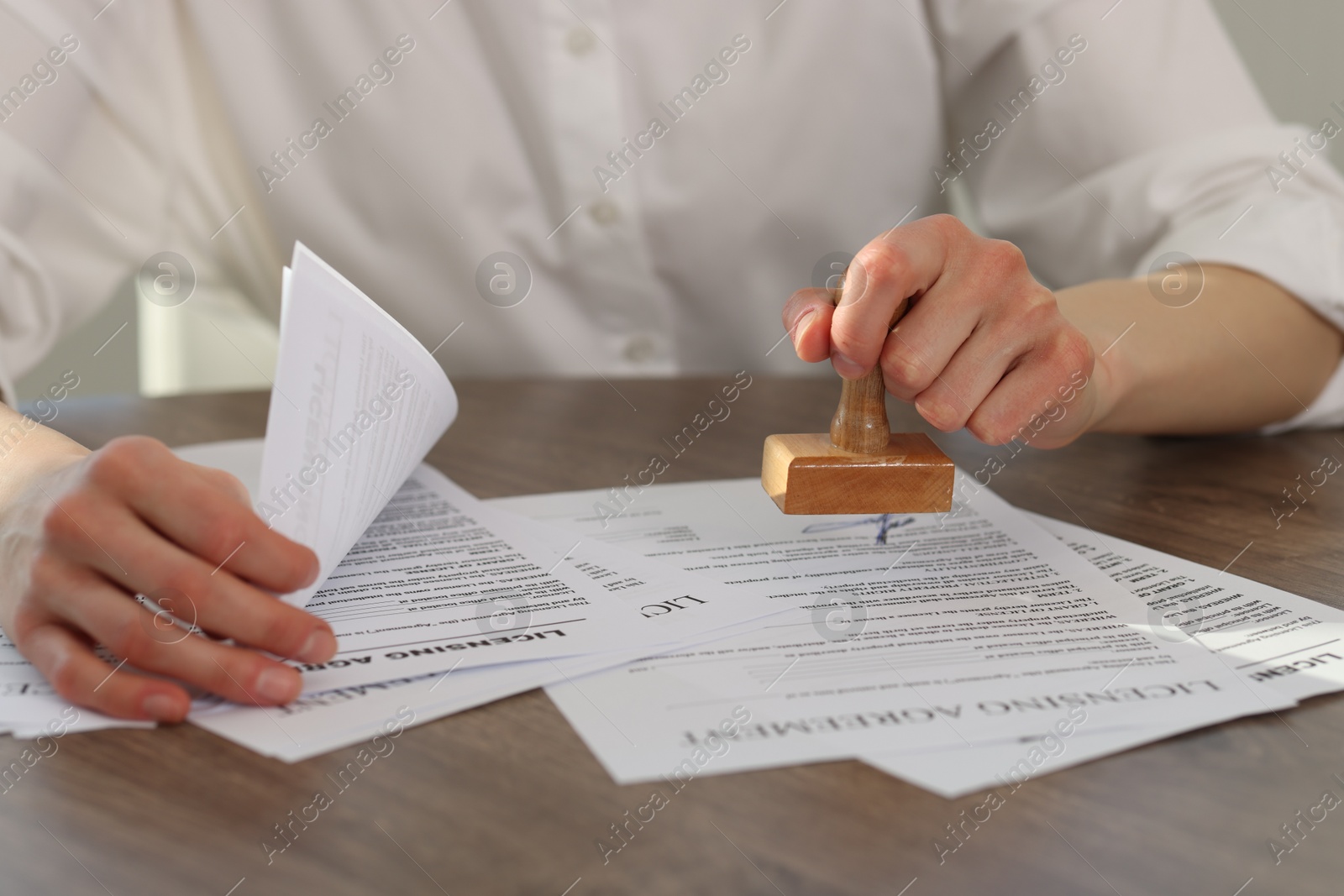 Photo of Woman stamping licensing agreement document at wooden table indoors, closeup