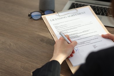 Photo of Woman signing licensing agreement document at wooden table indoors, closeup. Space for text