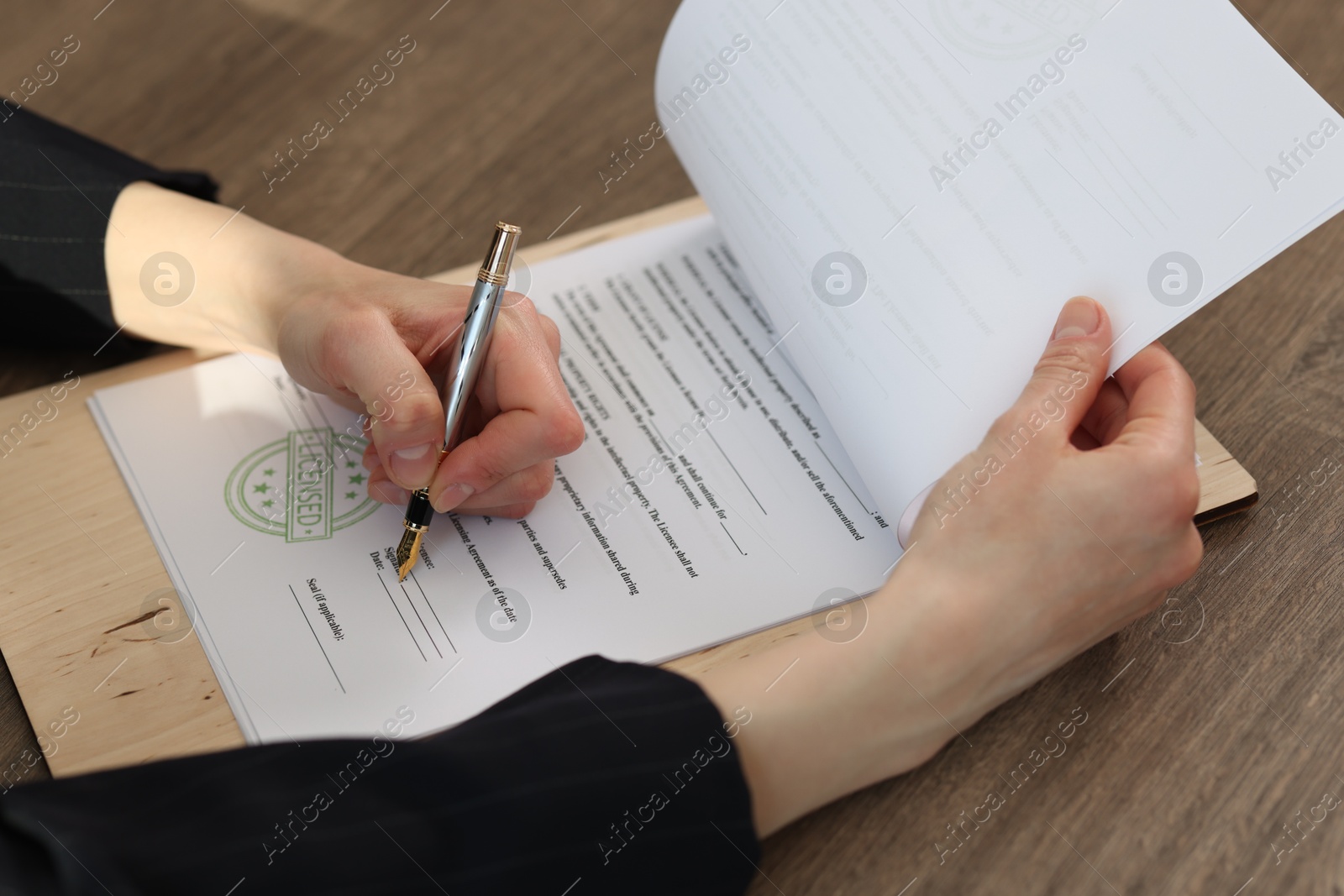 Photo of Woman signing licensing agreement document at wooden table indoors, closeup