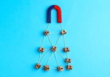 Image of Magnet attracting wooden cubes with human figures on light blue background, top view. Recruitment or customer acquisition