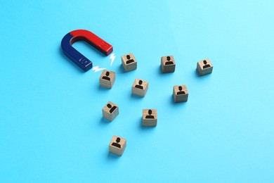 Image of Magnet attracting wooden cubes with human figures on light blue background. Recruitment or customer acquisition