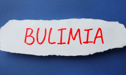 Image of Piece of paper with word Bulimia on blue background, top view